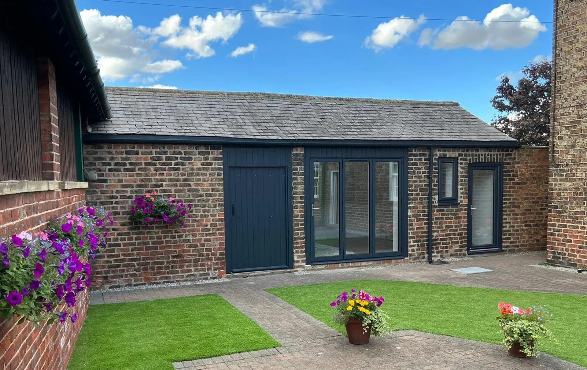 Converted outbuilding with anthracite bifold doors and landscaped garden, built by RGS Joinery and Building